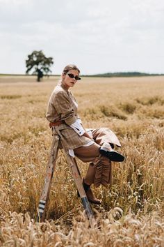 a woman sitting on top of a ladder in a wheat field with her eyes closed