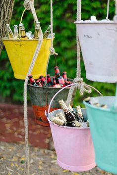 three buckets filled with wine bottles hanging from ropes next to a tree and bushes