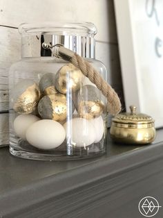 a glass jar filled with white and gold eggs on top of a fireplace mantel