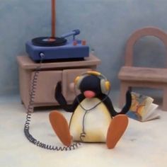 a toy penguin with headphones sitting on the floor next to a record player and chair