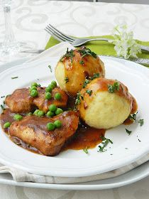 a white plate topped with meat covered in gravy and peas next to a fork