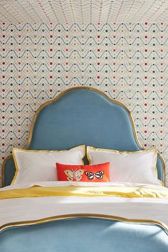 a bed with blue headboard and pillows in front of a wallpapered background