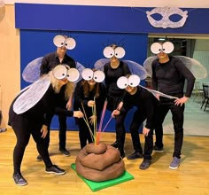 a group of people in costumes standing around a cake with eyes on it's face