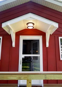 a red house with white trim on the front door and window above it is lit by an outdoor light