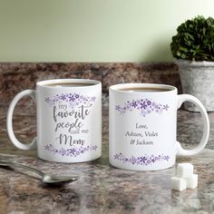 two coffee mugs sitting on top of a counter next to a potted plant