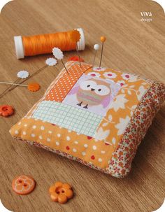 an orange and white patchwork pillow sitting on top of a wooden table next to sewing needles