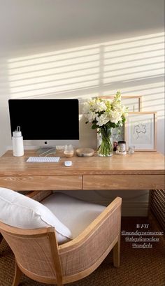 a wooden desk with a computer on it and flowers in the vase next to it