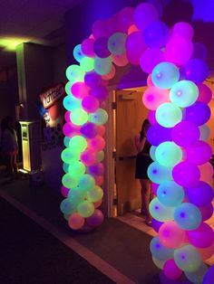 an arch made out of balloons is lit up with purple and green lights in the background