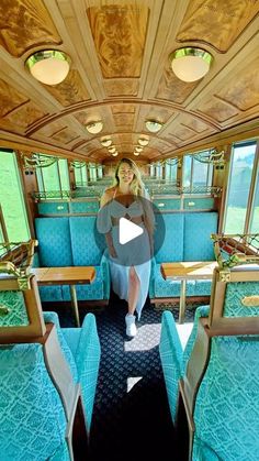 a woman standing in the middle of a train car with blue seats and wood trim