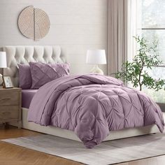 a bed in a bedroom with purple comforter and pillows