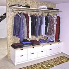 an organized closet with clothes hanging on the wall and drawers below it, along with a rug