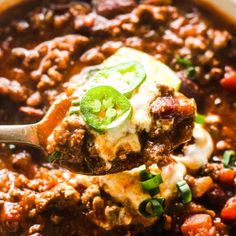 a spoon full of chili and ground beef soup with sour cream on top, garnished with green onions