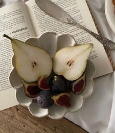 two pieces of fruit in a bowl on top of an open book with spoons