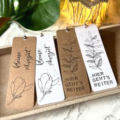 three bookmarks with handwritten words on them sitting in a box next to a potted plant