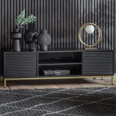 a black entertainment center with gold accents and vases on top, in front of a striped wall