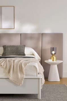 a white bed sitting next to a table with a lamp on it's side