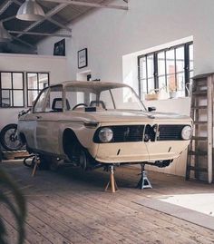 an old car sitting on top of a wooden floor next to a ladder in a garage