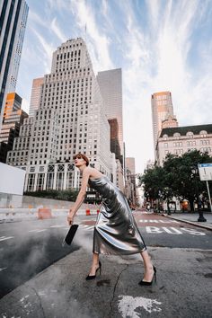 a woman is walking across the street in a silver dress and high heeled shoes