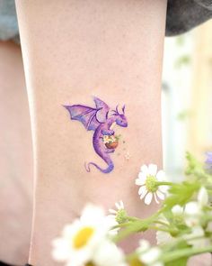 a small purple dragon tattoo on the right side of the leg, with daisies in front of it