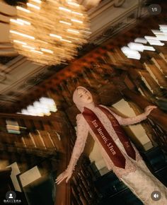 a mannequin wearing a red and white sash in front of a chandelier