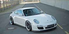 a white sports car parked on the side of a road next to a fence and building