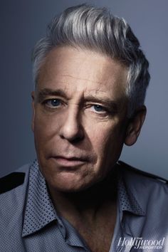 an older man with grey hair and blue eyes is looking at the camera while wearing a shirt