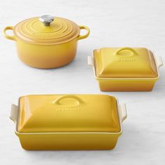 three yellow casserole dishes with lids and handles on a white countertop next to each other