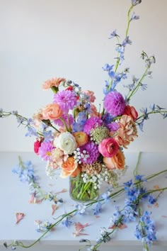 a vase filled with lots of colorful flowers on top of a white table next to blue and pink flowers