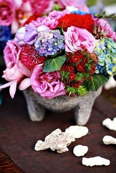 a vase filled with lots of flowers sitting on top of a wooden table next to white rocks