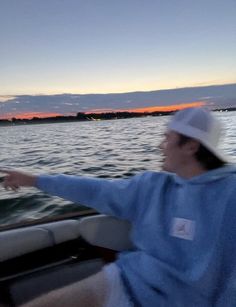 a man on a boat in the water pointing at something with his hand and wearing a hat