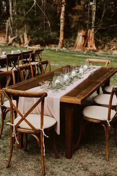 an outdoor table set up with white linens and wooden chairs for guests to sit at