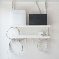 a white wall with some wires attached to it and an electronic device on the shelf