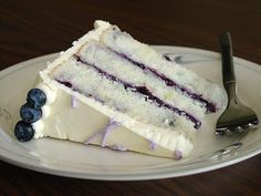 a slice of cake on a plate with blueberries and a fork next to it