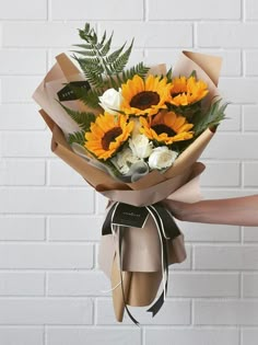 a bouquet of sunflowers wrapped in brown paper and tied to a brick wall