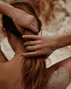 a woman with white powder on her face and hands touching her hair while she is covered in gold glitter