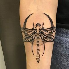 a dragonfly tattoo on the arm with a crescent moon in the middle and a scallop