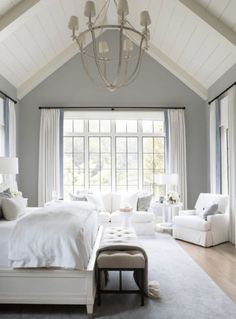 a bedroom with white furniture and large windows in the ceiling is lit by a chandelier