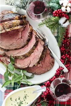 sliced roast beef on a white platter with red berries and wine