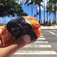 a person holding up a piece of food on the street with palm trees in the background