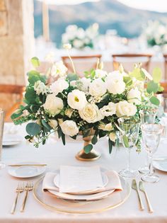 a table set with white flowers and place settings