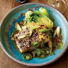 a blue plate topped with fish and veggies next to a glass of wine