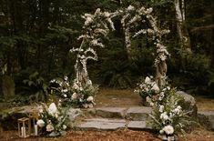 an outdoor ceremony setup with white flowers and greenery on the ground in front of trees