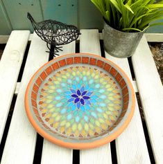 an orange and blue plate sitting on top of a wooden table next to a potted plant