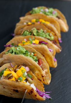 several tacos are lined up on a black surface with condiments in the middle