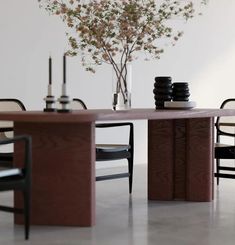 a dining room table with chairs and a vase on top of it, in front of a white wall