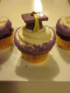 three cupcakes with purple frosting and a graduation cap on top are sitting on a white plate