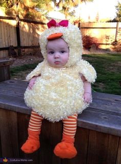 a baby in a chicken costume sitting on a bench