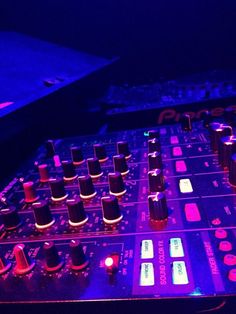 an electronic mixing board lit up with purple light in the dark, and blue lighting behind it