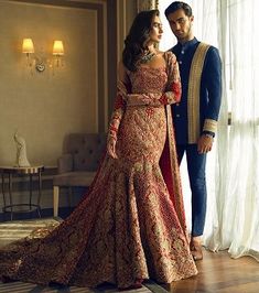 a man and woman standing next to each other in front of a window wearing wedding dresses