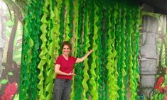 a woman standing in front of a green curtain with flowers on it and palm trees behind her